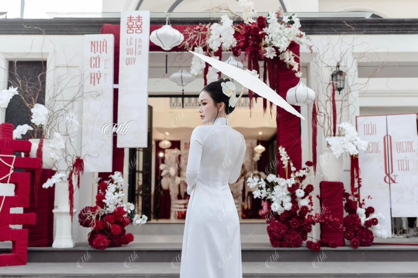 Cô dâu áo dài trắng trước cổng hoa đỏ trắng lễ vu quy