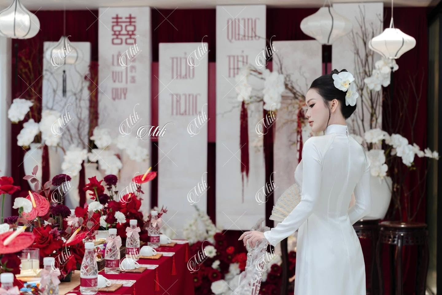 Cô dâu áo dài trắng bên bàn lễ gia tiên trang trí hoa đỏ