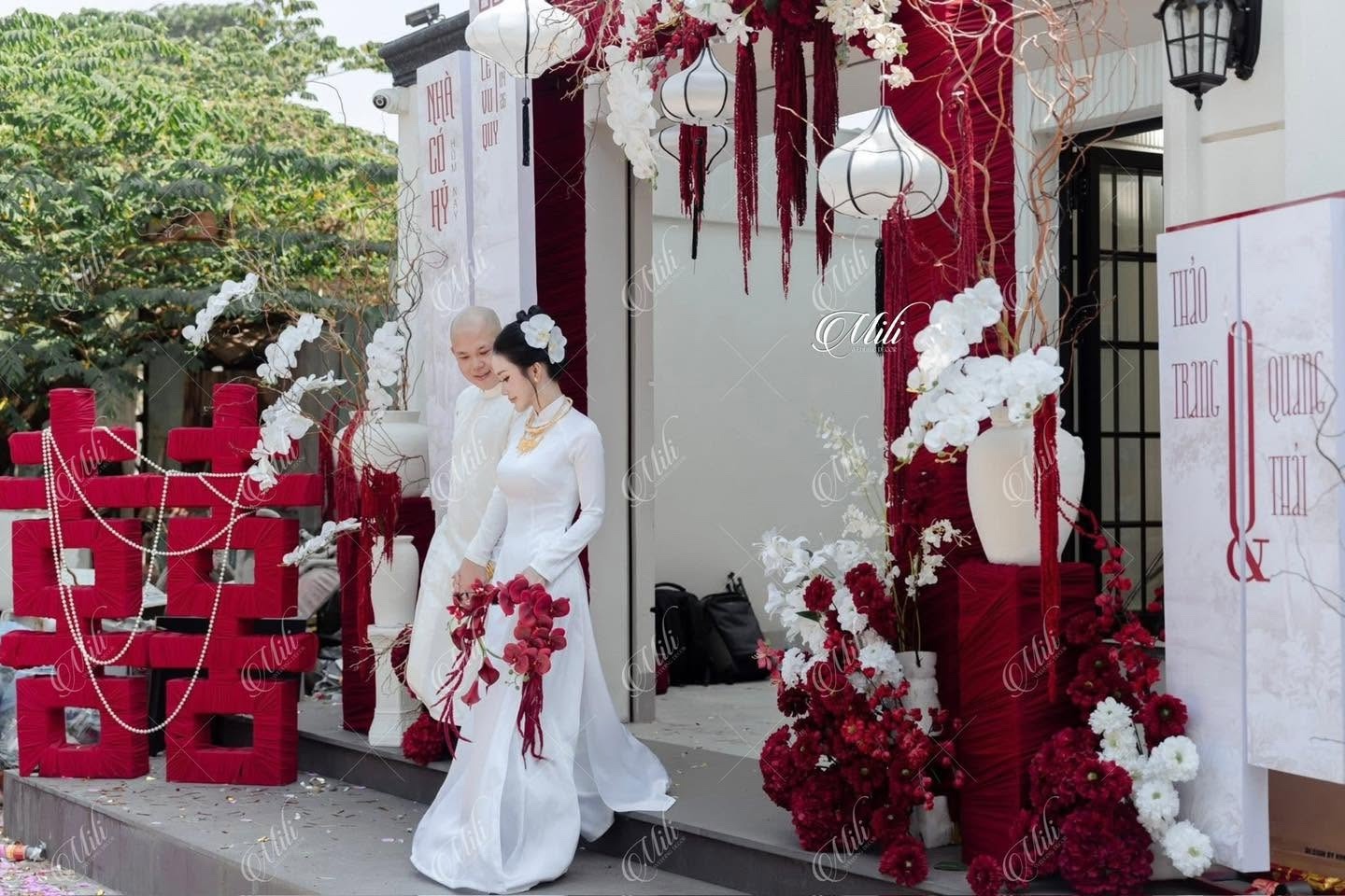Cô dâu chú rể áo dài trắng bên chữ hỷ và cổng hoa