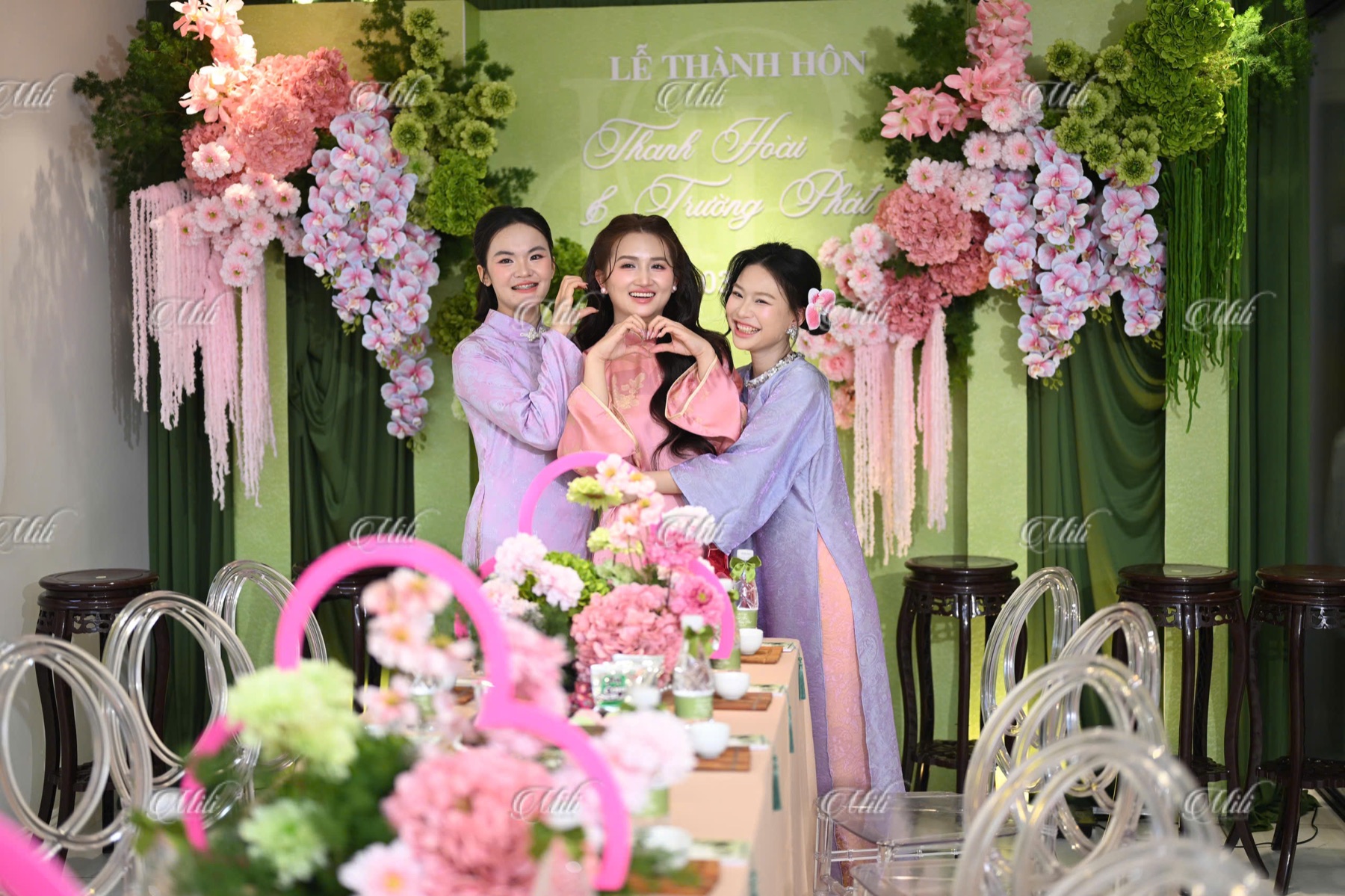Cô dâu và bạn bè chụp ảnh trước phông lễ xanh lá hồng phấn